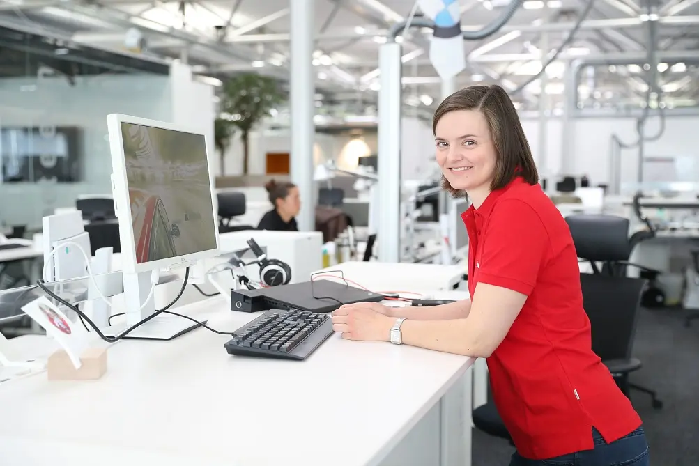 Smiling woman in red polo shirt working at a desk in a modern office