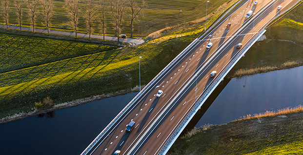 Traffic moving across a bridge with a river and fields in the background