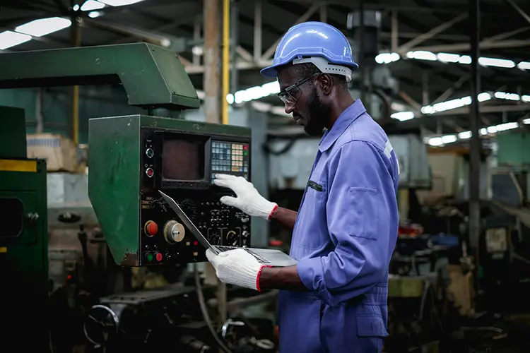 Person on a laptop at a vehicle manufacturing plant watching assembly line