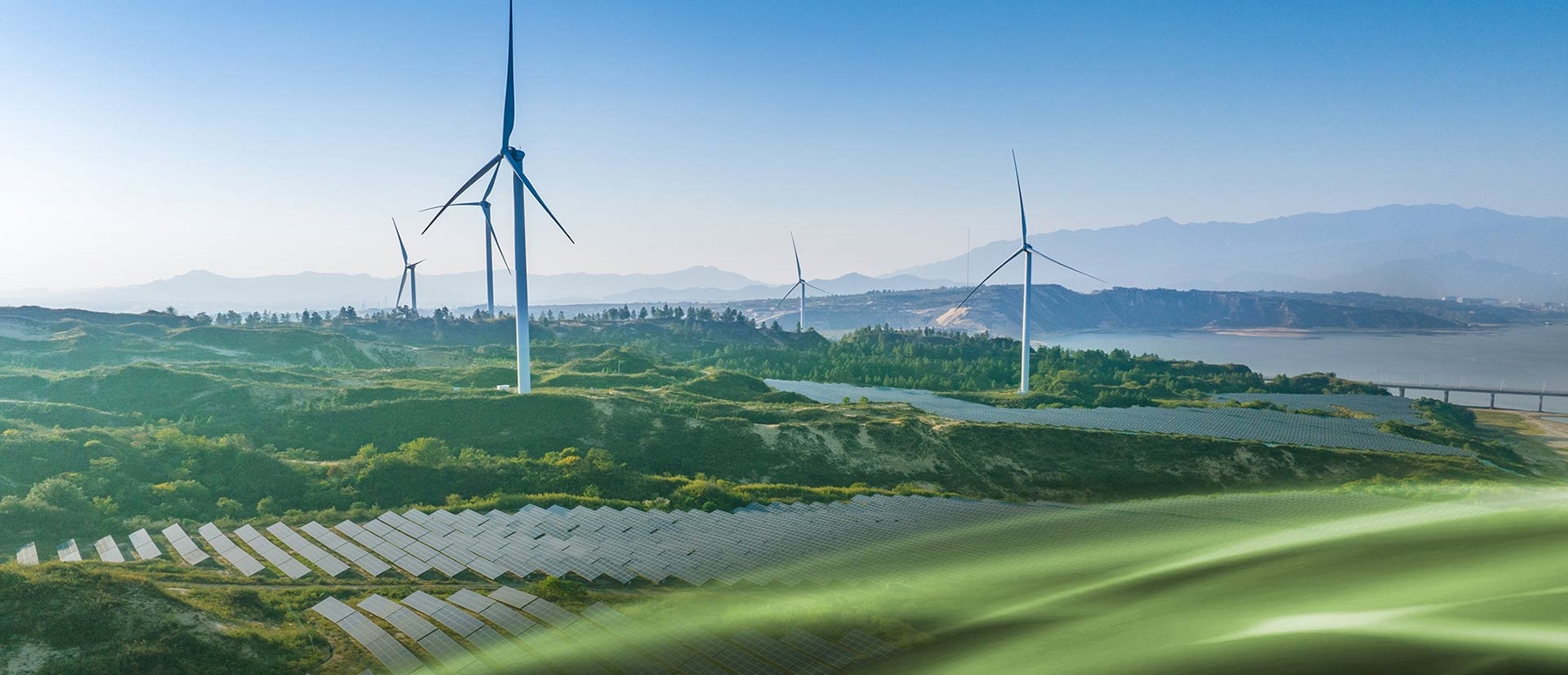 Landscape featuring wind turbines, solar panels, and rolling hills under a clear sky