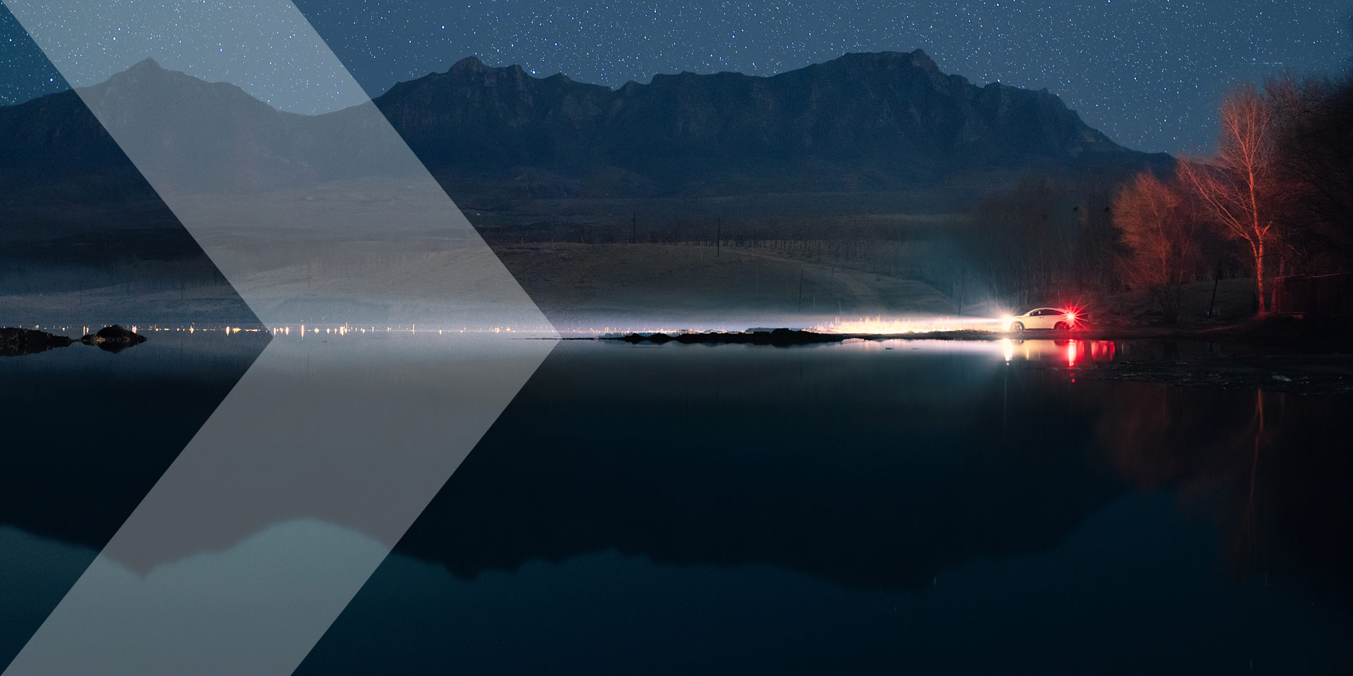 Vehicle at dusk with lights on and mountains in the background, chevron coming in from the left