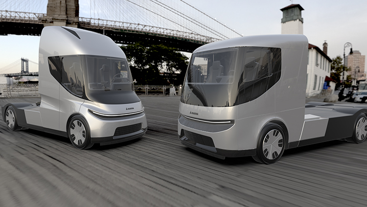 Two electric truck cabs sitting on a road with a suspension bridge in the background