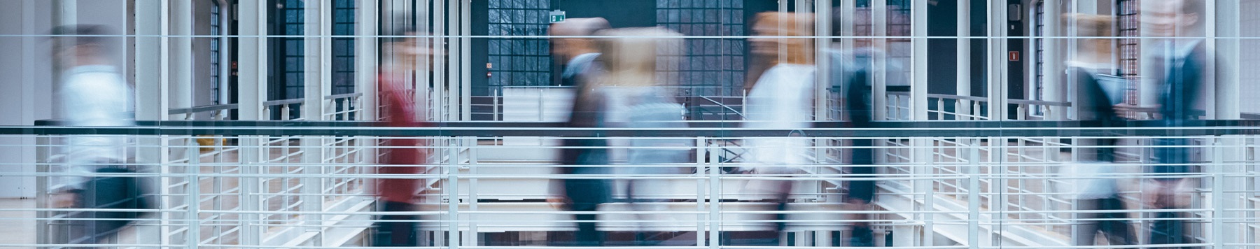 Blurred motion of people walking across a modern office walkway with glass railings