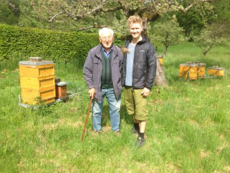 Alessandro Heuberger with his grandfather standing beside their bee hives in a field