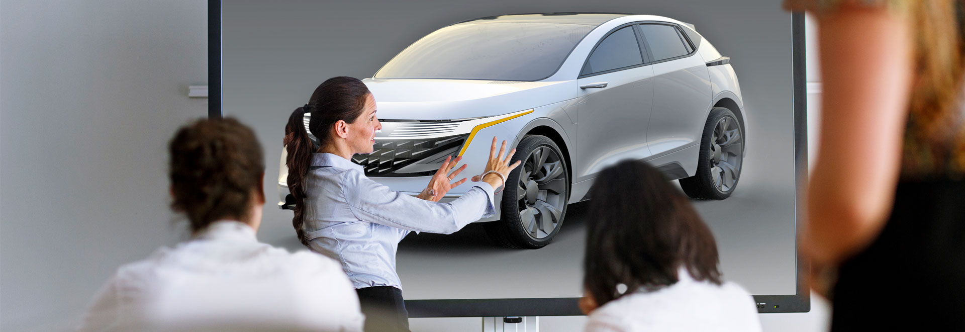 A Woman is showing 3 persons a car on a screen